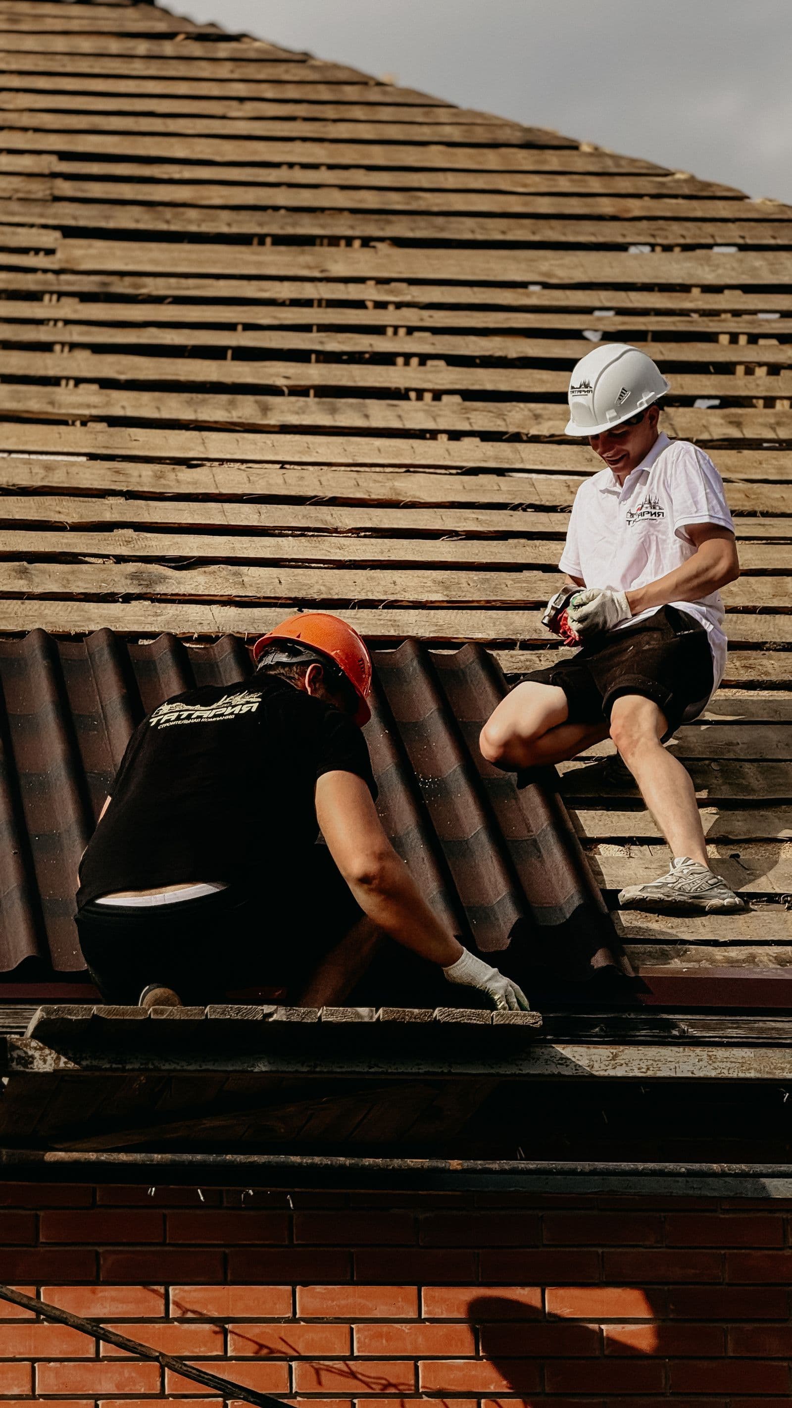 Roofers in hard hats repairing tiles on a pitched roof